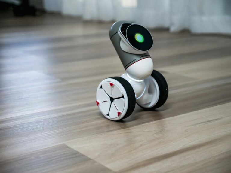 A close-up of a modern, wheeled robot with a digital interface, on a wooden floor.