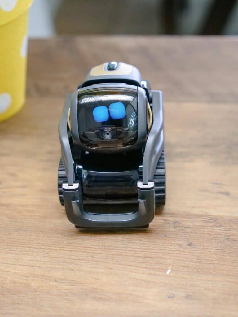 A small, innovative robot toy displaying blue digital eyes on a wooden tabletop.